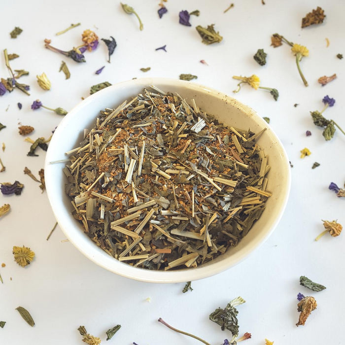 Abundance herbal tea mix in a white bowl with dried herbs scattered around on a light background