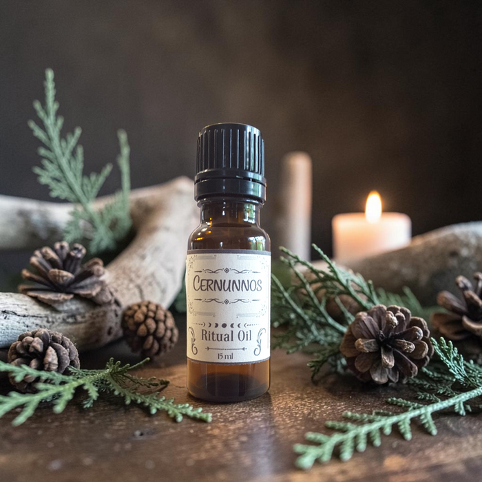 A small amber glass bottle of Cernunnos Ritual Oil with a black cap and cream label, styled on a rustic wooden surface with pine branches, pinecones, driftwood, and a lit candle in the background.