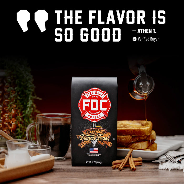 A bag of FDC Fire Department Coffee French Toast stands on a wooden table in a breakfast scene, with a glass of black coffee, a stack of French toast on a plate with syrup, cinnamon sticks, and a small pitcher of milk. Large text at the top reads “THE FLAVOR IS SO GOOD” with “ATHEN T.