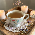 Teacup with floral design on a wooden tray with candles and dried flowers