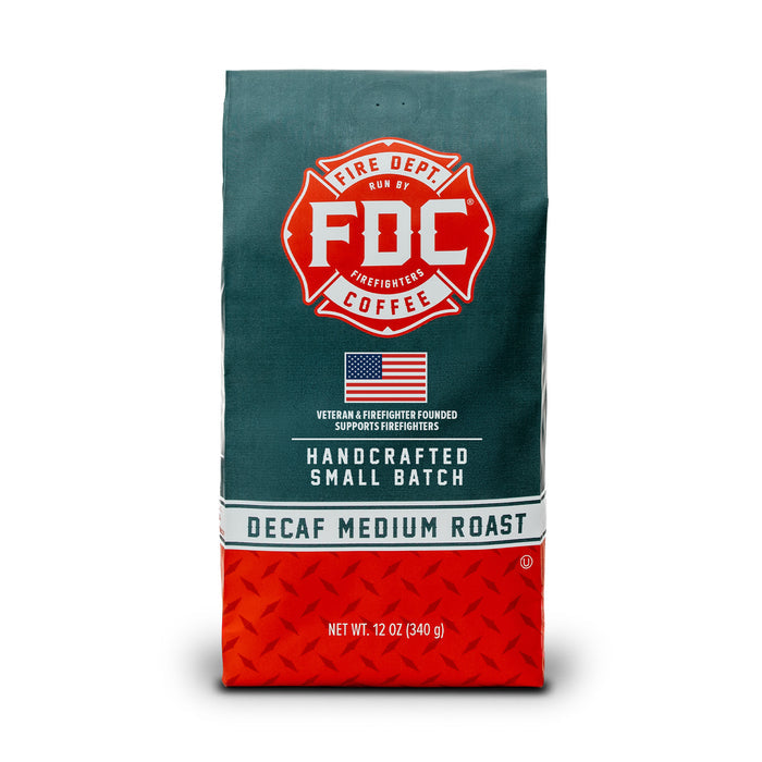 A 12 oz bag of FDC Fire Department Coffee Decaf Medium Roast, featuring a dark teal upper half with a red fire department emblem and white text, and a red diamond-plate patterned lower half.