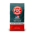 A 12 oz bag of FDC Fire Department Coffee Decaf Medium Roast, featuring a dark teal upper half with a red fire department emblem and white text, and a red diamond-plate patterned lower half.