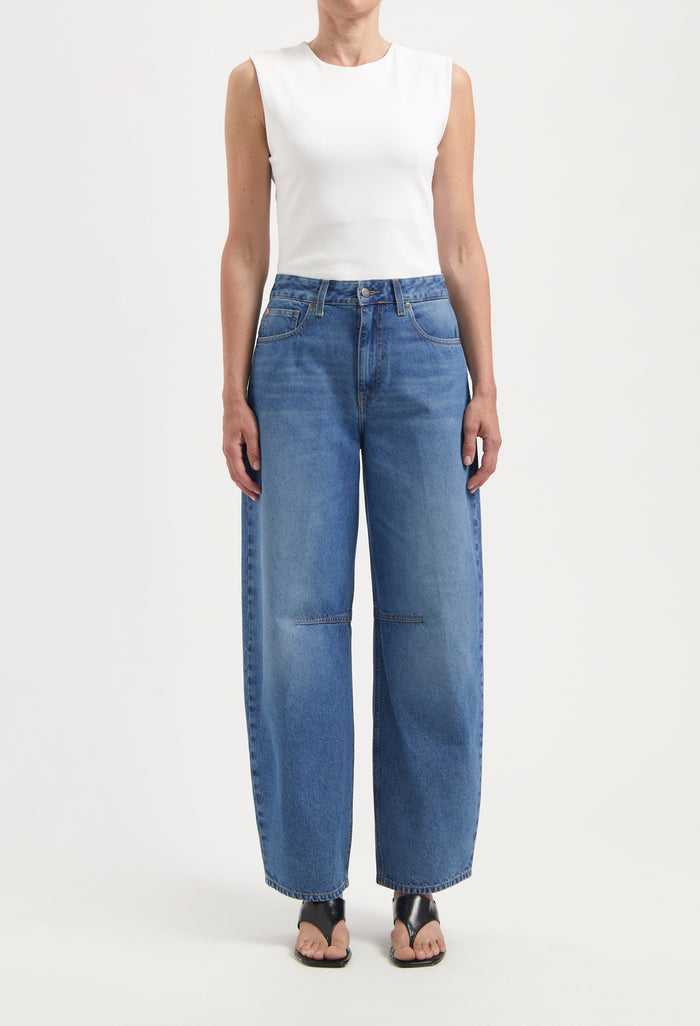 Wide-legged blue denim jeans with pockets and high waist, paired with a sleeveless white top and black sandals.