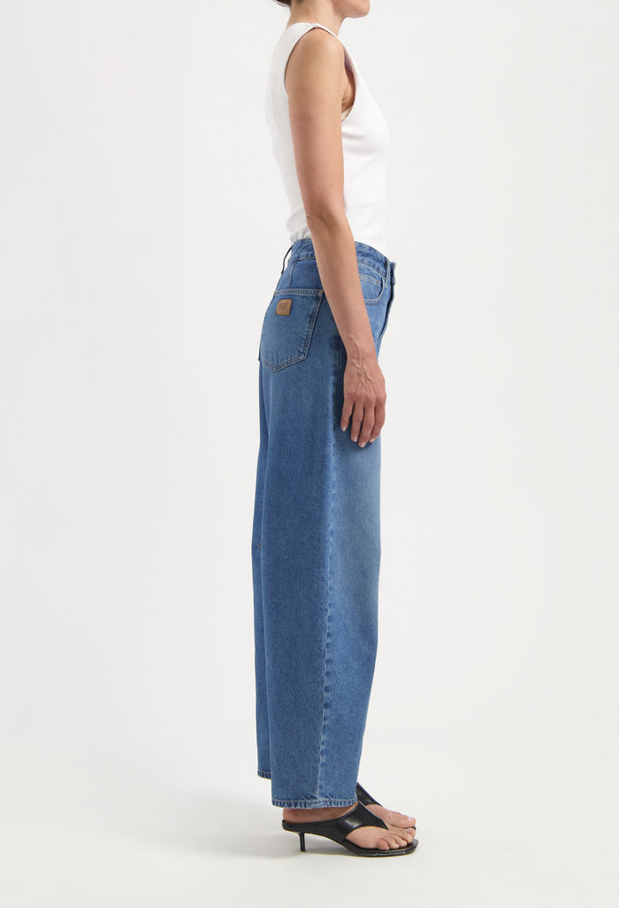 Side view of woman wearing high-waisted blue denim jeans with straight-leg fit and white sleeveless top paired with black heels.