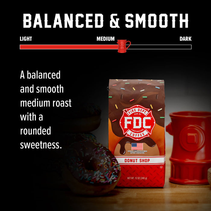 A bag of FDC Coffee medium roast donut shop coffee stands on a wooden surface with a red fire hydrant-shaped mug and a chocolate donut in a dark, styled setting. Text at the top reads 'BALANCED & SMOOTH' with a roast slider graphic.