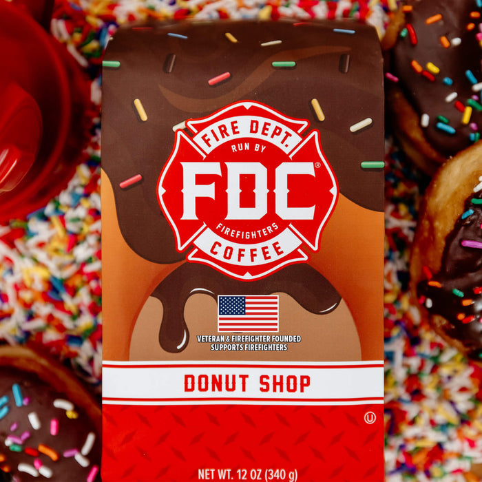 A 12-ounce package of Fire Department Coffee's Donut Shop Coffee surrounded by rainbow sprinkles and donuts.