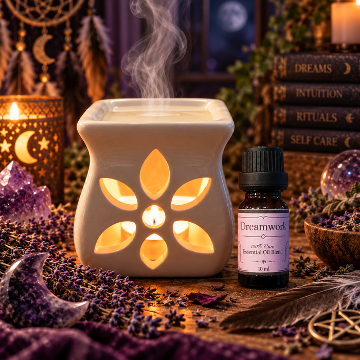 Dreamwork witchy diffuser blend alongside an essential oil burner on a wooden surface with lavender and amethyst crystals and a candle and stacked books in the background