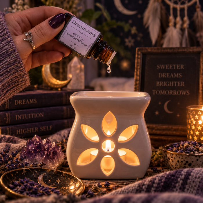 Dreamwork witchy diffuser blend being poured into an essential oil burner on a wooden surface with lavender and amethyst crystals and stacked books in the background