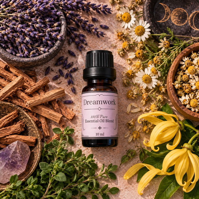 Dreamwork witchy diffuser blend on a tan surface surrounded by lavender, sandalwood sticks, chamomile flowers and ylang ylang flowers