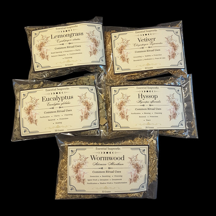 Five clear plastic bags of energy cleansing herbs for witchcraft with cream-colored labels are arranged on a solid black background. The labels feature botanical illustrations and names of the herbs: Lemongrass, Vetiver, Eucalyptus, Hyssop, and Wormwood.