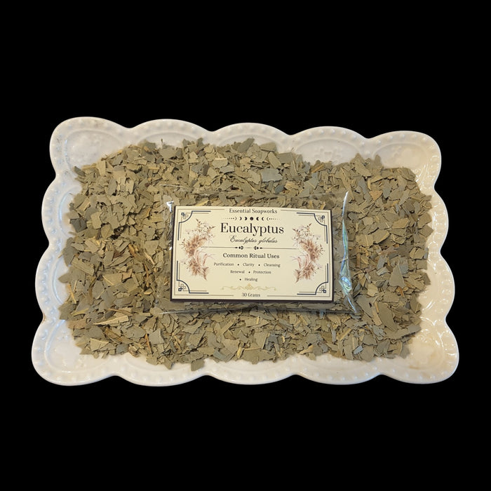 A package of Eucalyptus sits in the center of a white scalloped ceramic dish filled with loose dried eucalyptus leaves, set against a solid black background.