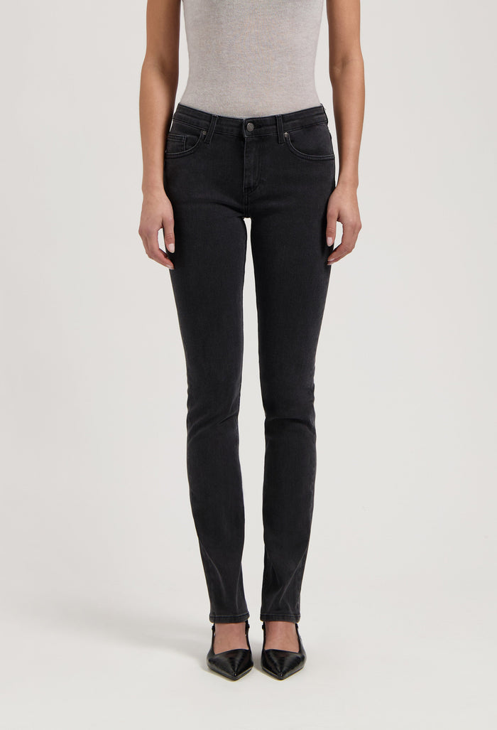 Woman wearing fitted black denim jeans paired with a light gray sleeveless top and pointed black shoes.