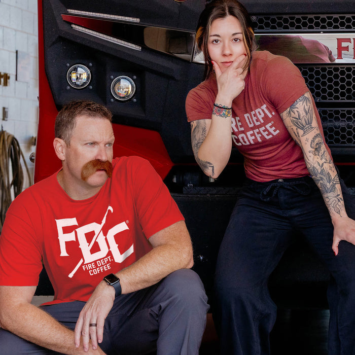 Two people wearing red 'FDC' shirts sitting in front of a fire truck.