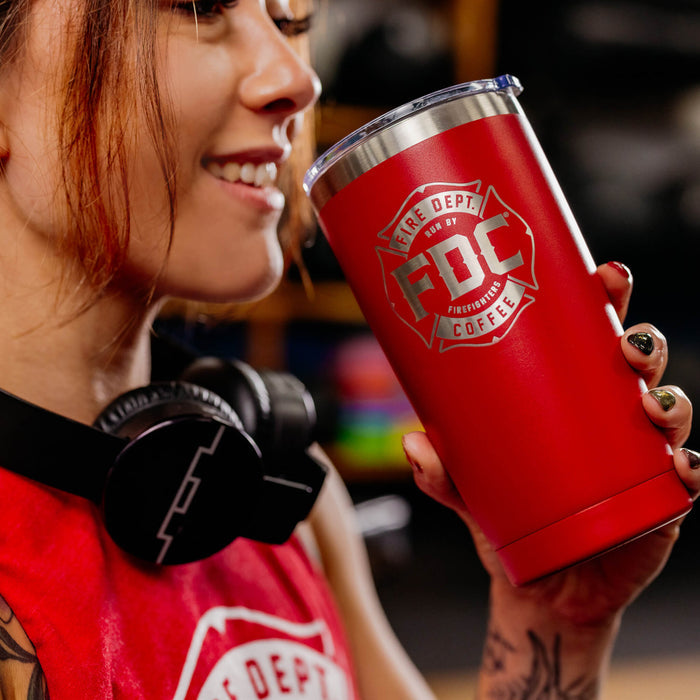 A woman drinking out of a red Fire Department Coffee Maltese Cross Tumbler.