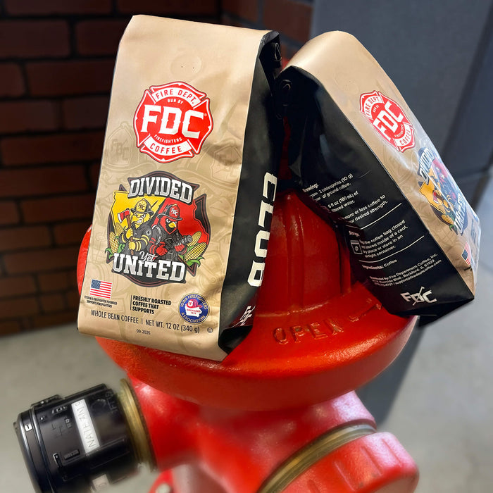 Two bags of FDC Coffee Company 'Divided and United' whole bean coffee are draped over a bright red fire hydrant in an outdoor setting with a brick wall in the background.