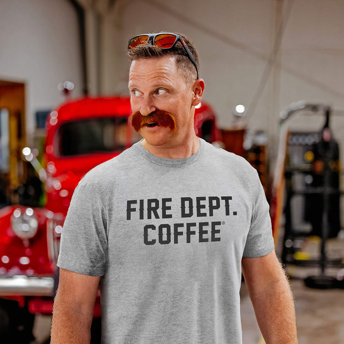 Man wearing a gray 'Fire Dept. Coffee' text t-shirt in a fire station with a vintage red truck in the background.