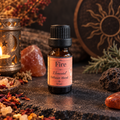 A 10 ml amber glass bottle of 'Fire' Elemental Diffuser Blend with a black cap and pink label, styled on a dark stone surface with a lit candle, crystals, dried flowers, and a decorative sun disc in the background.