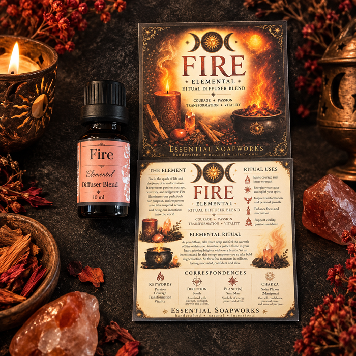 A small essential oil bottle labeled 'Fire Elemental Diffuser Blend' is shown with its branded card packaging and an informational card on a dark tabletop, surrounded by candles, dried botanicals, crystals, and autumn leaves.