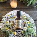 Gentle Surrender Emotional Wellness Oil on a doily on a wooden surface with chamomile flowers