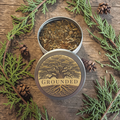 Grounding incense with tree design on lid, surrounded by greenery and pine cones on wooden surface
