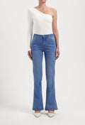 One-shoulder white top with long sleeve paired with high-waisted blue flare jeans, styled with white pointed heels.