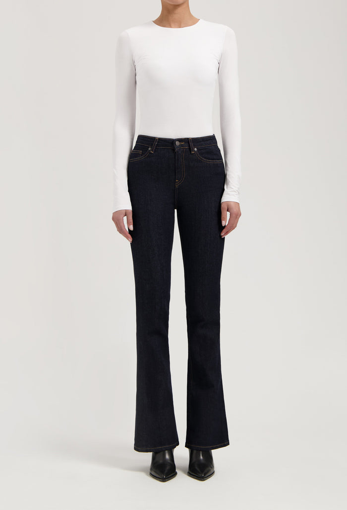 Woman wearing dark blue bootcut jeans with a white long-sleeve fitted top, showcasing casual chic style.