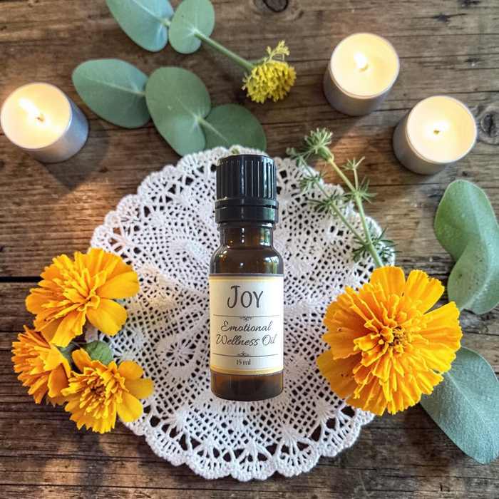 Joy Emotional Wellness Oil on a doily on a wooden surface with orange flowers, greenery and candles