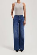 Woman wearing wide-leg blue denim jeans paired with a sleeveless light gray top in a minimalist style.