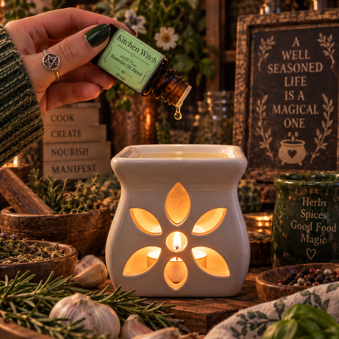 Kitchen Witch essential oil diffuser blend being poured into an essential oil burner on a wooden surface with peppermint and rosemary with a candle and stack of books in the background