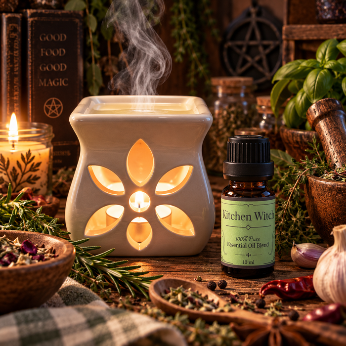Kitchen Witch essential oil diffuser blend with an essential oil burner on a wooden surface with peppermint and rosemary and other various spices with a candle in the background