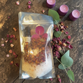 Love Spell Bath Ritual Kit with bath salts, rose petals, ritual oil, tealight candles and rose quartz crystal on a wooden surface