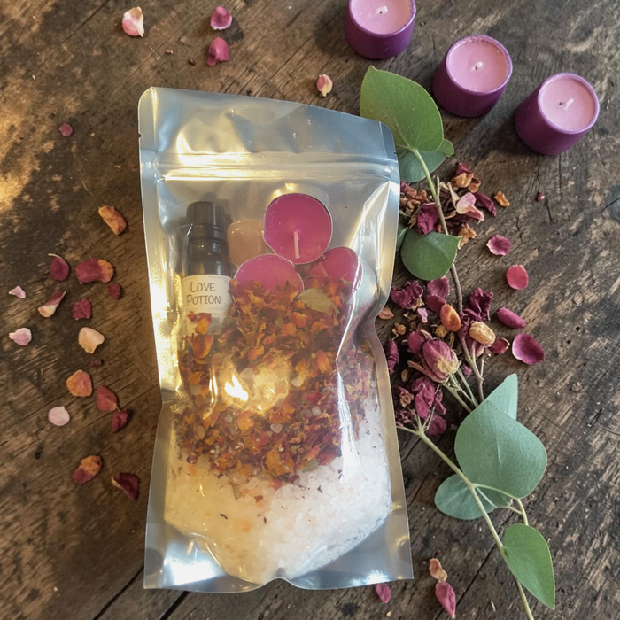 Love Spell Bath Ritual Kit with bath salts, rose petals, ritual oil, tealight candles and rose quartz crystal on a wooden surface