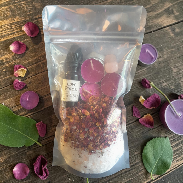 Love Spell Bath Ritual Kit with bath salts, rose petals, ritual oil, tealight candles and rose quartz crystal on a wooden surface