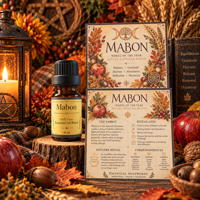 A bottle of Mabon ritual pure essential oil blend and its matching illustrated dispenser card are displayed on a rustic wood slice with autumn props including acorns, a candle, and books.