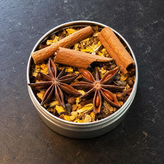 A round metal tin filled Mabon loose incense including cinnamon sticks, star anise, and dried citrus peel, photographed from above on a dark textured surface.