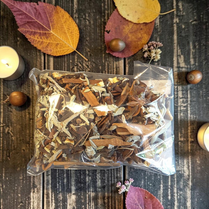 Mabon simmer pot herbs including cinnamon sticks, bark, and light sage-like pieces, placed on a dark rustic wooden surface with autumn leaves, acorns, and candles around it.