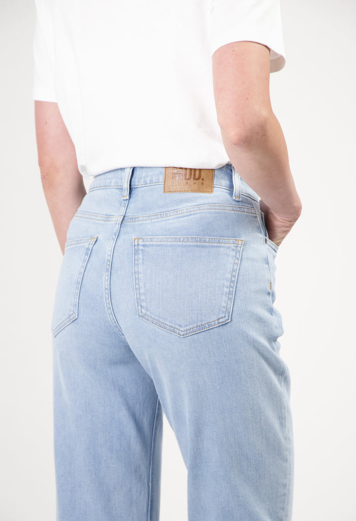 Light blue MUD Jeans crafted from organic cotton, featuring a relaxed fit and subtle stitching, paired with a white T-shirt.