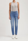 Woman wearing light gray sleeveless top and high-waisted blue jeans, paired with white sneakers, isolated on white background.