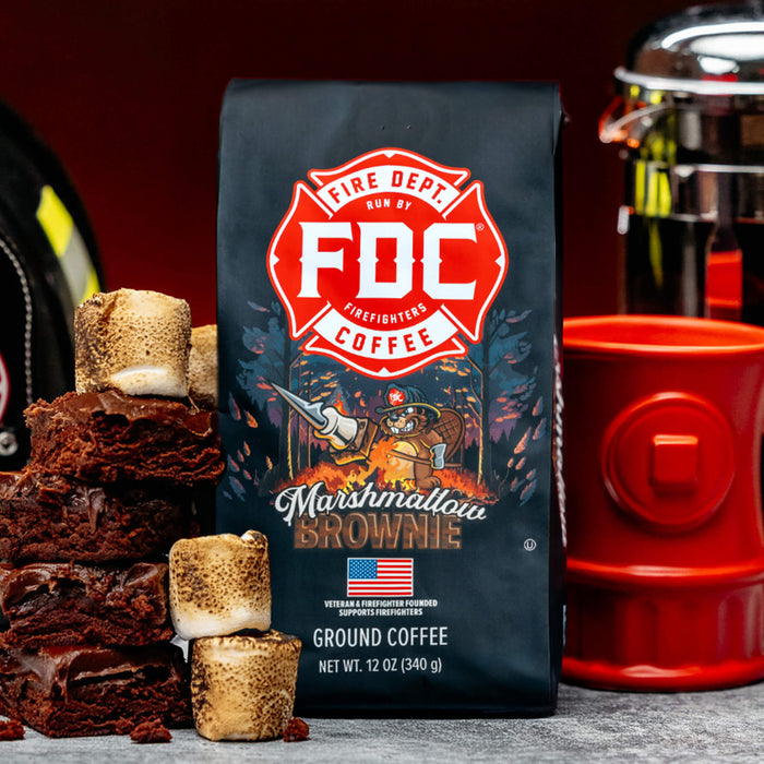 A bag of Fire Department Coffee's 12 oz Marshmallow Brownie Coffee set on a table with a pile of brownies and toasted marshmallows next to it.