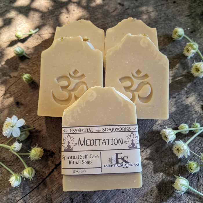 four bars of meditation soap on a dark wooden surface with white flower buds