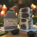 Obsidian crystal soap with decorative packaging on a table with blurred candles in the background