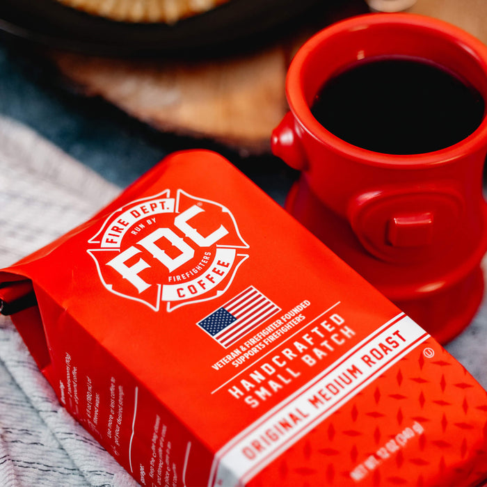 A bag of Original Medium Roast Coffee laying on a table next to a Fire Hydrant Coffee Mug full of coffee.