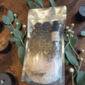 Protection Bath Ritual Kit with bath salts, herbs, ritual oil, tealight candles and snowflake obsidian crystal on a wooden surface