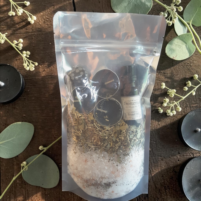Protection Bath Ritual Kit with bath salts, herbs, ritual oil, tealight candles and snowflake obsidian crystal on a wooden surface