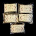 Five clear plastic bags of witchy herbs for protection arranged on a black background. The bags contain loose dried herbs and feature vintage-style cream labels with floral illustrations and text including Rosemary, Cinquefoil, Rue, Motherwort, and Angelica Root.