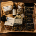 A Samhain Ritual Kit filled with tea, essential oils, soaps, and herbal accessories on a dark wood background. Visible items include multiple bags of herbal tea blends labeled Rue, Motherwort, St.