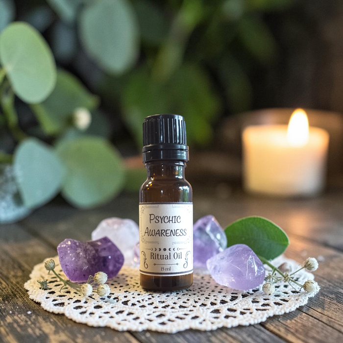A small amber glass bottle labeled 'Psychic Awareness Ritual Oil' sits on a white lace doily with purple crystals and green leaves, with a blurred lit candle in the background.