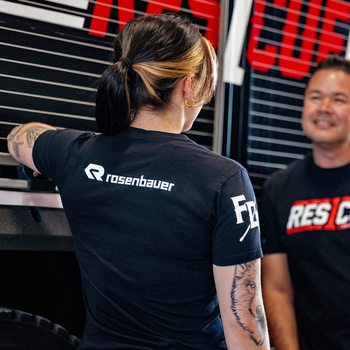 A woman standing talking to a man next to a fire truck wearing the Rescue1 Shirt, featuring the Rosenbauer logo on the back of her shirt.