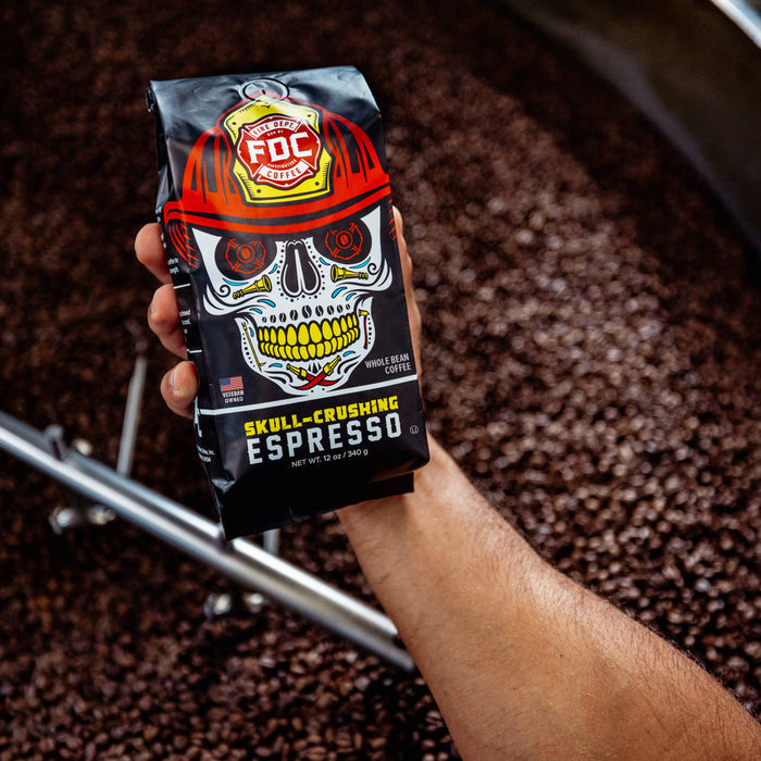 An image of FDC's Skull Crushing Espresso being held over a vat of roasted coffee beans.