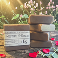 Restoration & Renewal Emotional Wellness Soap on a wooden surface with flowers in the background.